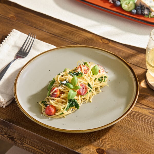 An Acopa Keystone porcelain plate with pasta, tomatoes, and basil on a wooden table.