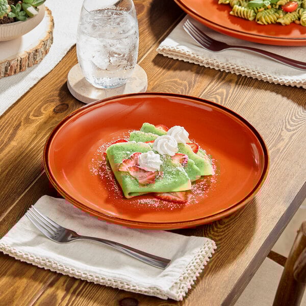 A table with two Acopa Keystone Sedona Orange porcelain coupe plates of food on it.