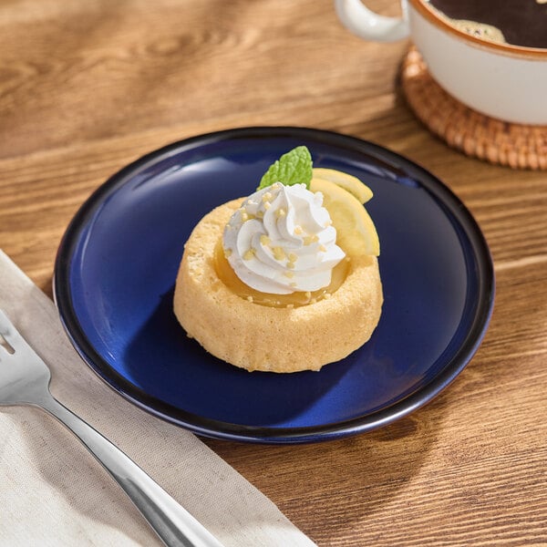 A small round blue porcelain coupe plate holding a dessert with whipped cream and fruit garnish.