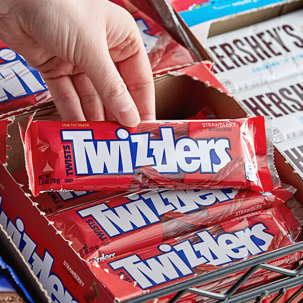 A hand holding a box of TWIZZLERS Strawberry licorice on a counter in a convenience store.