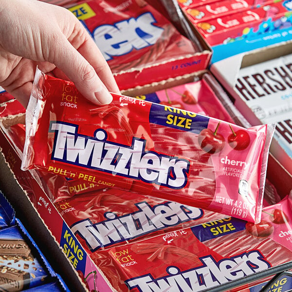 A hand holding a package of TWIZZLERS King Size Pull n' Peel Cherry Licorice.