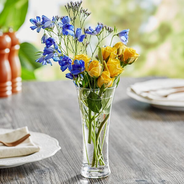 An Acopa glass bud vase with flowers on a table.