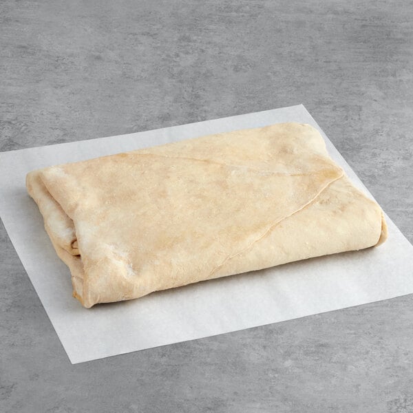 A folded sheet of raw puff pastry dough on a piece of parchment paper.