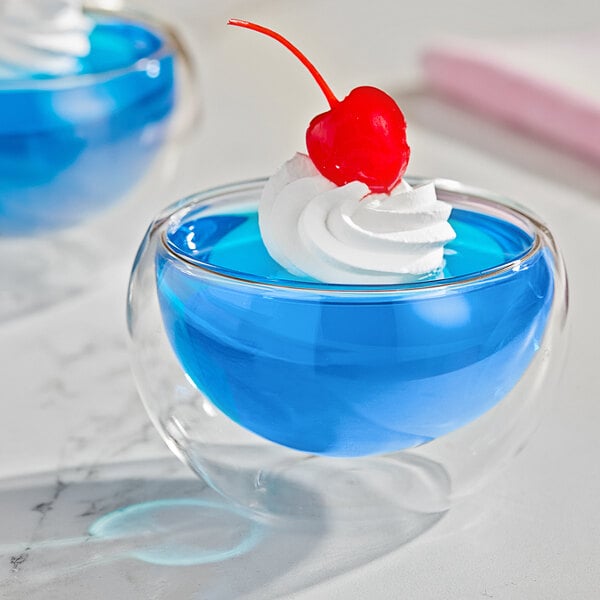 A glass cup with blue JELL-O and a cherry on top.