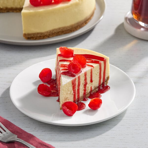 A slice of cheesecake topped with maraschino cherry halves and cherry syrup on a white plate.