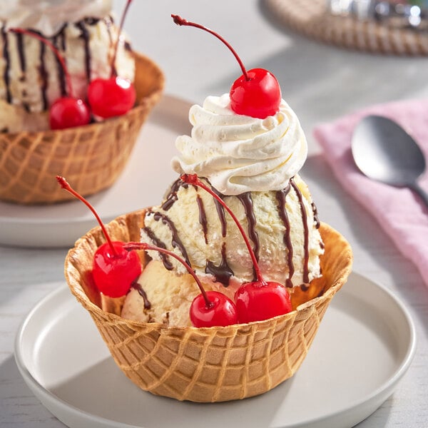 A bowl of vanilla ice cream in a waffle cup topped with maraschino cherries, whipped cream, and chocolate syrup.