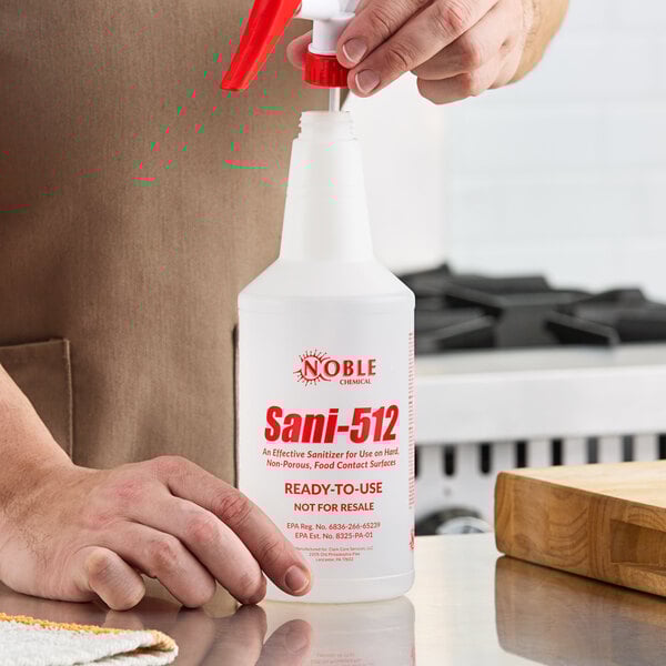 A hand holding a white Noble Chemical Sani-512 bottle.