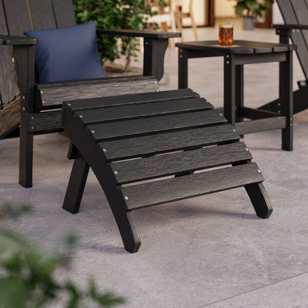 A black Lancaster Table & Seating Adirondack chair and footrest on a patio.