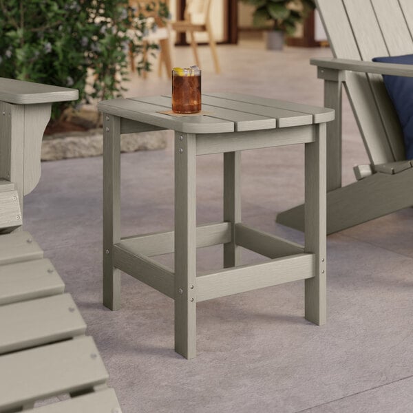 A Lancaster Table & Seating gray high impact polystyrene side table on a patio with a drink on it.