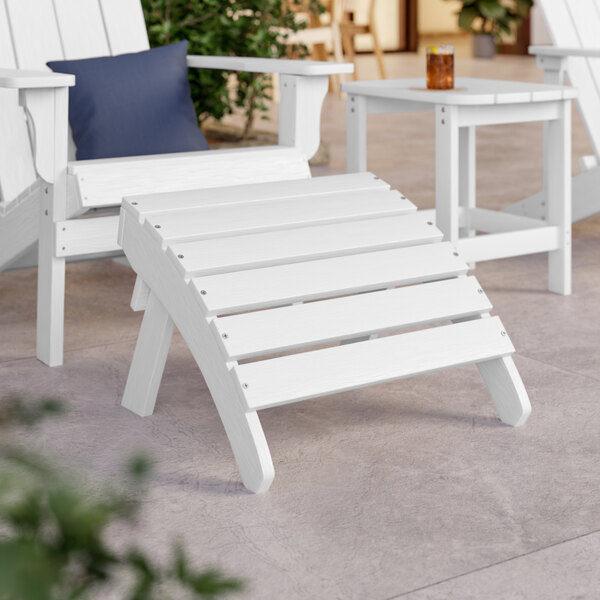 A white Adirondack footrest with slats next to a white Adirondack table.