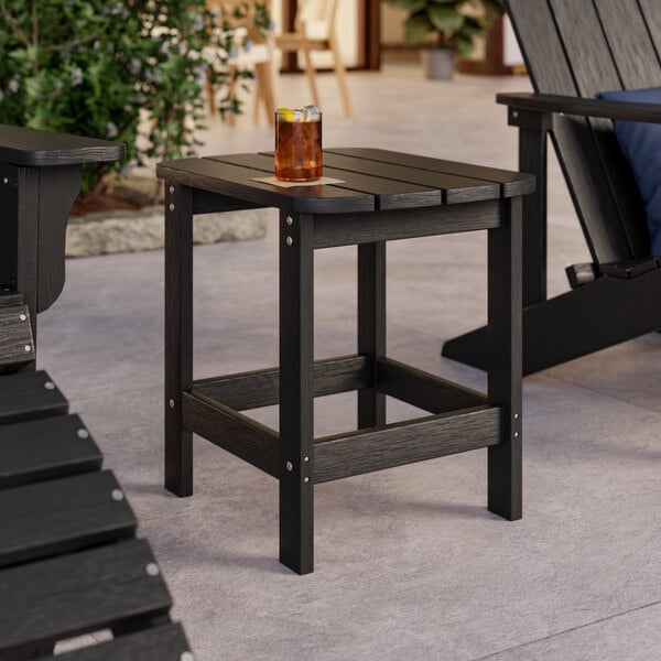 A black Lancaster Table & Seating Adirondack side table on an outdoor patio with a drink on it.