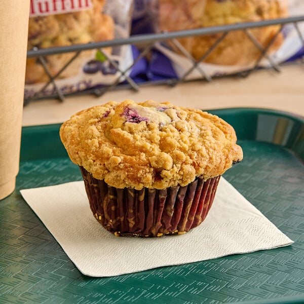 An individually wrapped blueberry crumb muffin on a tray.