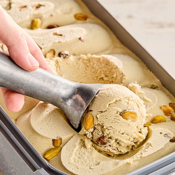 A hand scooping G.S. Gelato Sicilian Pistachio gelato with a metal scoop.