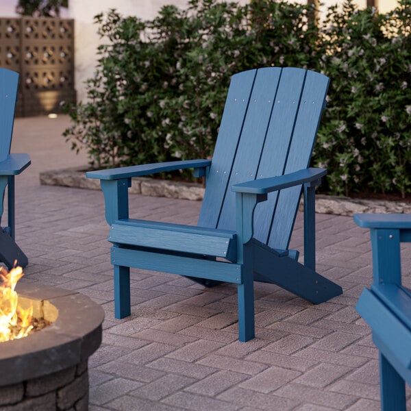 Two blue Lancaster Table & Seating Modern Adirondack chairs on a brick patio next to a fire pit.