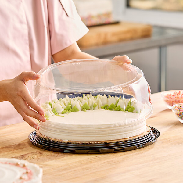 A woman holding a Baker's Lane cake in a clear plastic container with a scalloped clear lid.