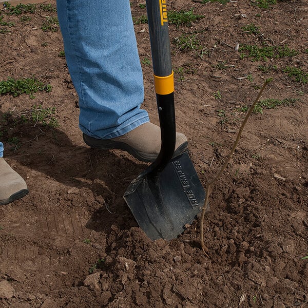 A person using a True Temper round point shovel with a yellow and black metal handle to dig in the dirt.
