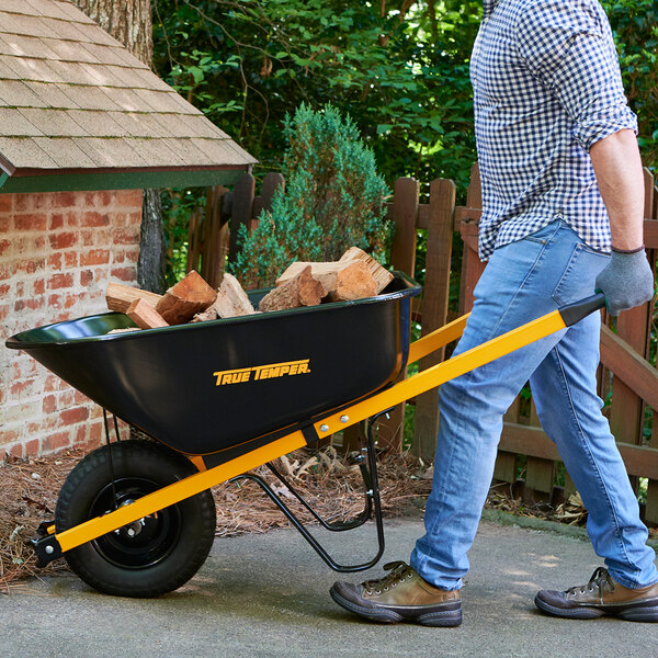 A man pushing a True Temper wheelbarrow full of wood.