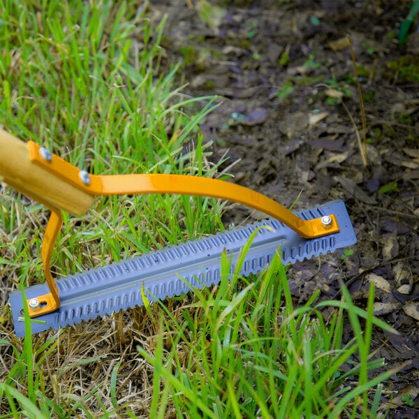 A steel weed cutter with a hardwood handle being used to trim grass and weeds.