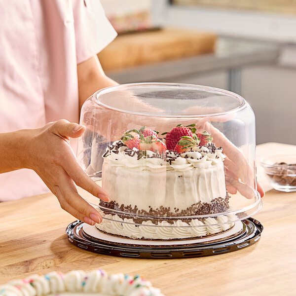 A woman placing a cake with strawberries and chocolate sprinkles into a Baker's Lane glass dome container.
