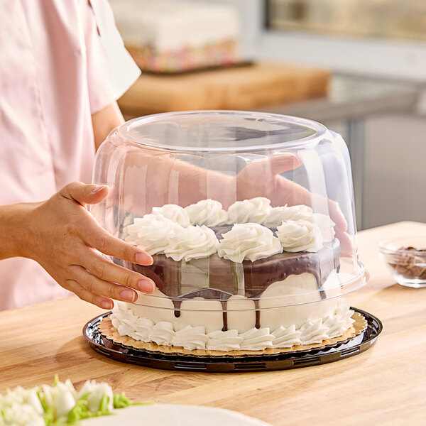 A woman holding a cake in a clear plastic dome display container.