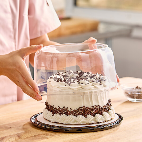 A woman holding a cake in a Baker's Lane glass cake display container with a clear scalloped dome lid.