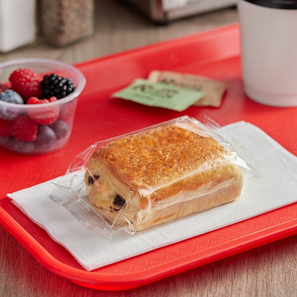 A Brioche Gourmet chocolate croissant wrapped in plastic on a red tray.