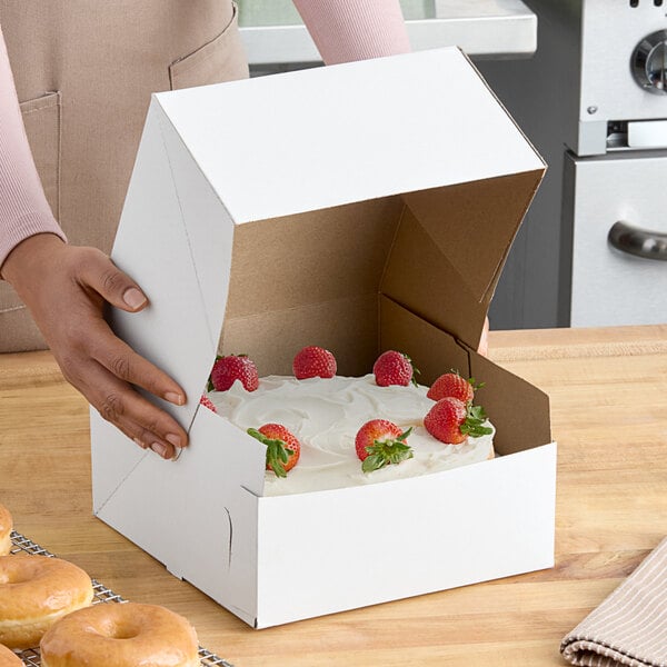 A woman opening a Baker's Lane white cake box to reveal a cake with strawberries on top.