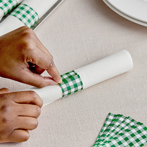 A person's hands wrapping a napkin with green and white checkered paper tape.