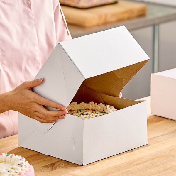 A person opening a white Baker's Lane cake box.
