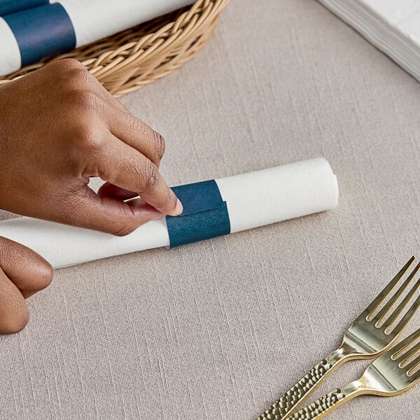 A hand cutting a blue paper napkin band with a knife.