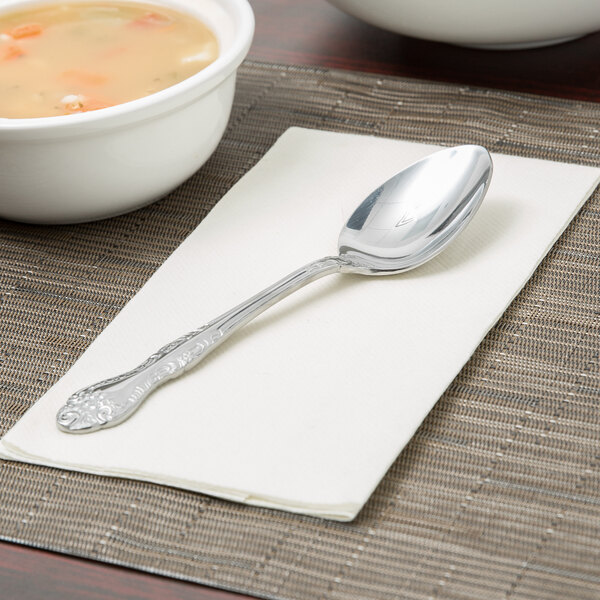 A Oneida Rosewood stainless steel oval bowl soup spoon on a napkin next to a bowl of soup.