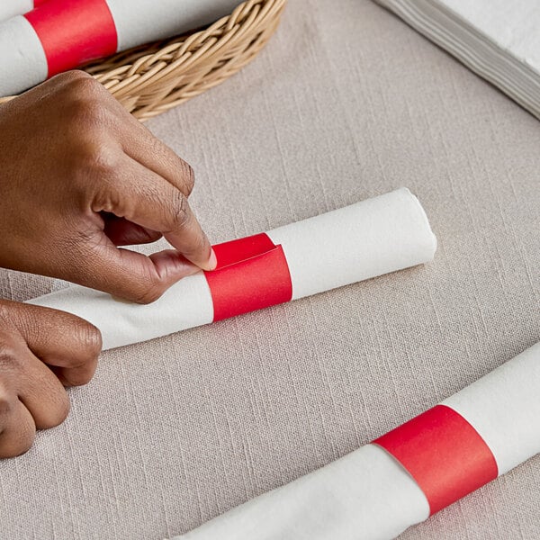 A person's hands wrapping a white napkin with a red Choice paper band.