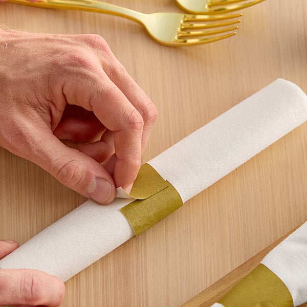 A person's hand using a Choice Gold Self-Adhering Paper Napkin Band to wrap a napkin.