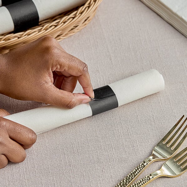 A person's hand using a knife to cut a black paper napkin band.