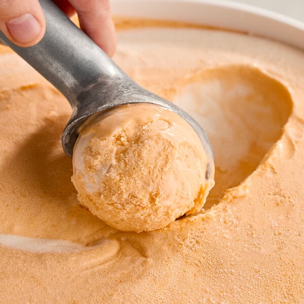 A hand scooping orange ice cream from a container.