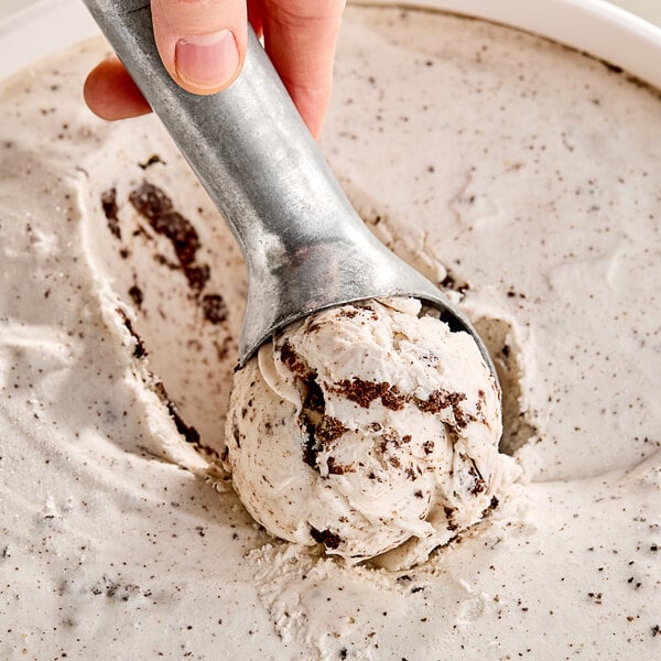A hand using a scoop to serve Klein's Cookies 'N Cream Ice Cream.