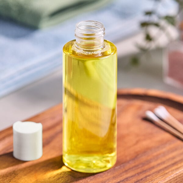 A 4 oz. clear PET cylinder bottle of yellow liquid on a wooden tray.