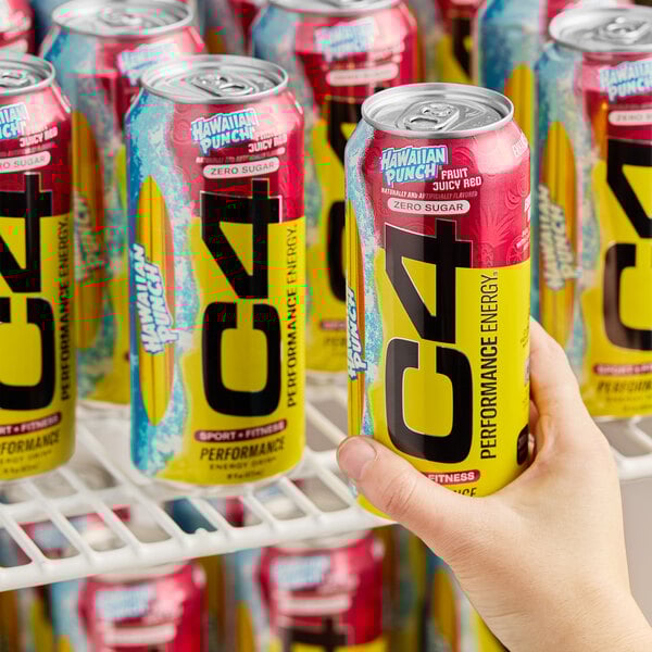 A 16 fl. oz. can of C4 Energy Hawaiian Punch Fruit Juicy Red energy drink being held in front of several identical cans on a refrigerator shelf.