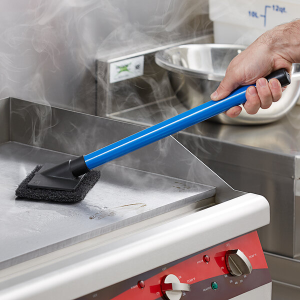 A hand using a blue Scrubble pad holder to clean a stove.