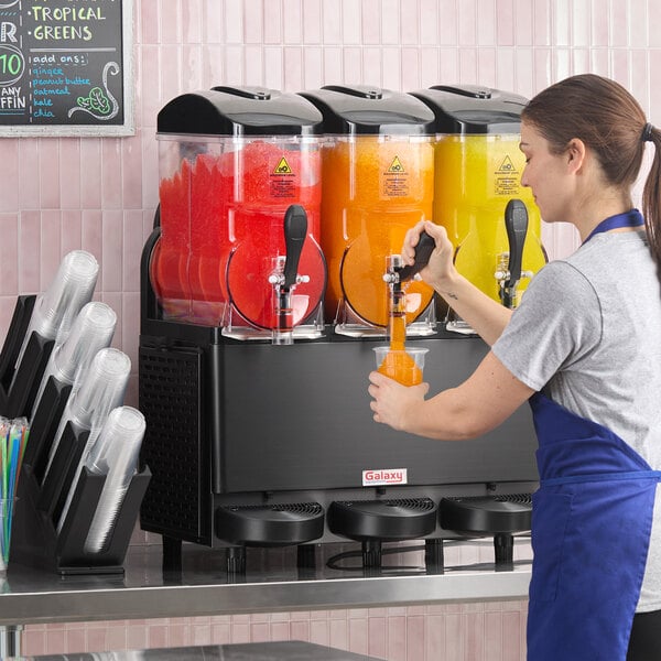 A triple 3-gallon pourover granita, slushy, or frozen beverage machine with three clear containers holding red, orange, and yellow frozen drinks.