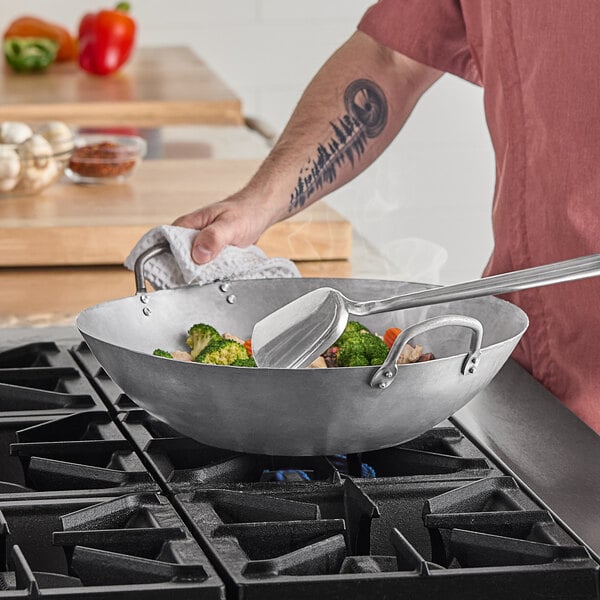 A man using an Emperor's Select carbon steel wok to cook vegetables on a gas stove.