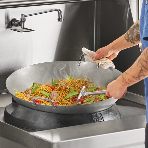 A large 24-inch carbon steel Cantonese wok being used to cook stir-fried noodles and vegetables.