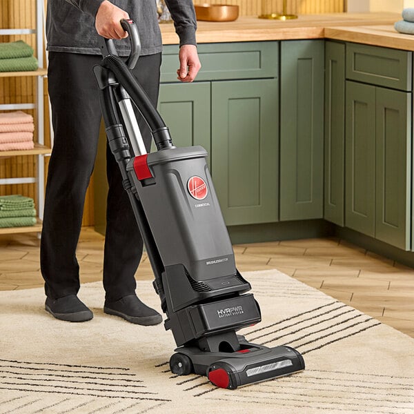 A person pushing a Hoover cordless upright vacuum cleaner in a living room.