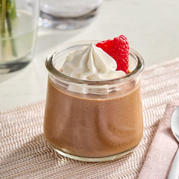 A glass jar of chocolate pudding with whipped cream and a raspberry on top.
