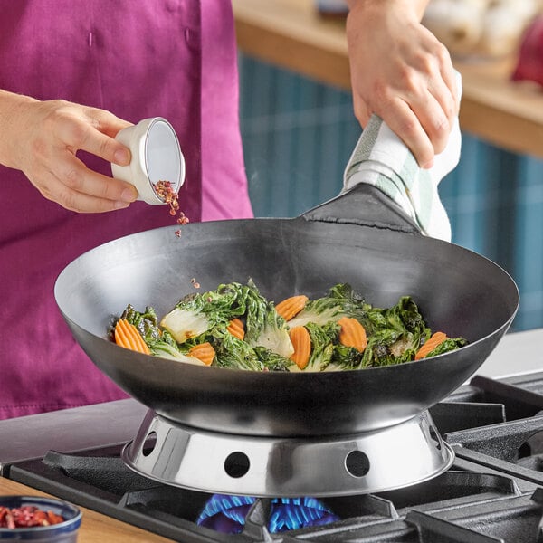 A 14-inch heavy-duty oxidized carbon steel Mandarin wok being used to stir-fry vegetables on a gas stove.