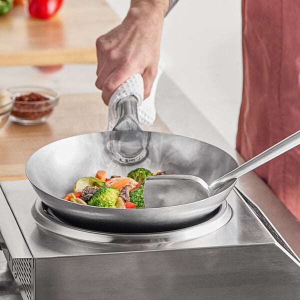A person cooking vegetables in an Emperor's Select carbon steel wok on a stove.