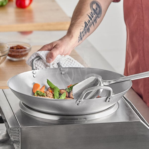 A person cooking food in an Emperor's Select carbon steel wok.
