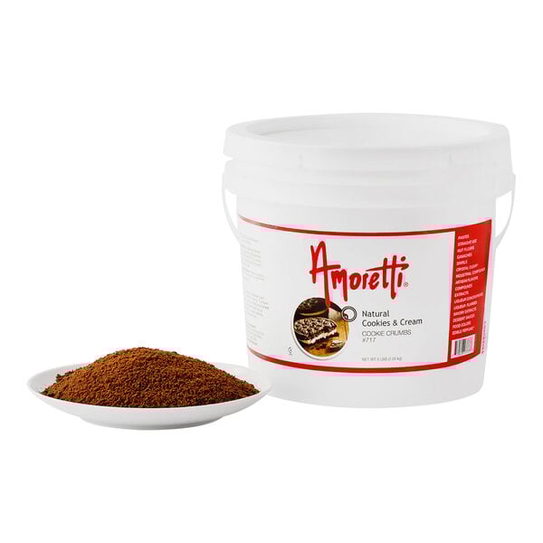 A white bucket of Amoretti Cookies & Cream Cookie Crumbs with a white label next to a bowl of brown cookie crumbs.