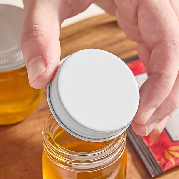 A person holding a 43/400 white metal lid on a jar of honey.