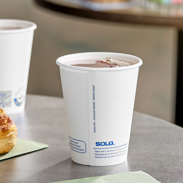 A white Solo ProPlanet paper hot cup filled with brown liquid sitting on a table next to a pastry.